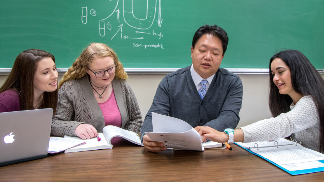 three students working at a table with a professor