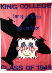 A red banner with a black airplane silhouette, blue text reading KING COLLEGE Serving the Nation in War and Peace, an emblem with two U.S. flags and the word LIBERTY, and CLASS OF 1944 at the bottom.