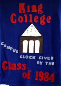 A blue banner with red and white letters reads: King College Class of 1984, with Campus clock given by the in smaller gray letters. The banner features a clock tower with Roman numerals.